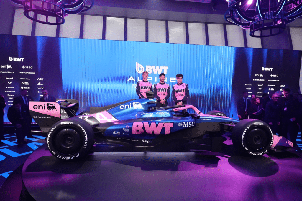 A studio shot of the 2026 Alpine A526 Formula One car, featuring the iconic blue and BWT pink livery with prominent MSC Cruises branding. Large white text reading "A526" is overlaid in the background. The car showcases the new 2026 regulation design, including a more compact body and refined aerodynamics, presented in a moody, industrial-style setting.
