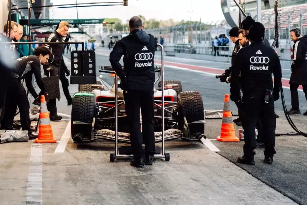 The Audi R26 F1 car in the pitlane during the 2026 Barcelona shakedown, featuring the Titanium and Lava Red livery with Revolut branding.
