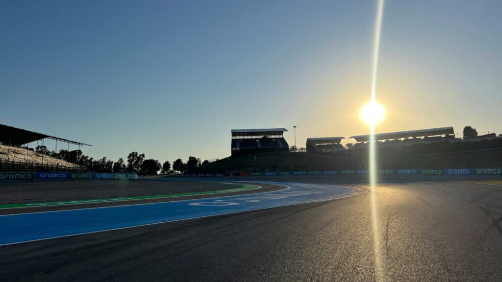 Sun setting over the curved track and grandstands of the Circuit de Barcelona-Catalunya stadium section with blue track curbing.