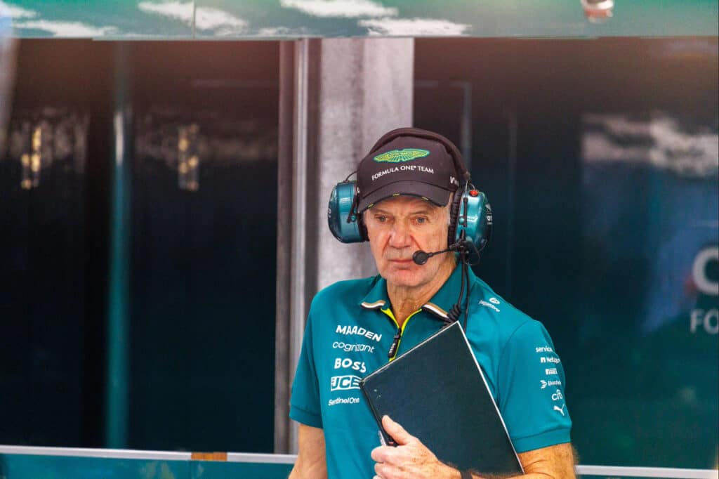 Adrian Newey at the Aston Martin pit wall, holding his notebook and wearing a team headset, representing his central role in the team's 2026 design philosophy.