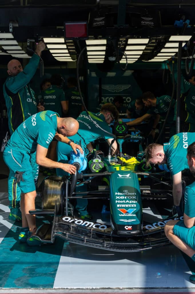 A detailed side profile of the 2026 Aston Martin in the pit lane, focusing on the engine cover and battery housing area where faults were detected.