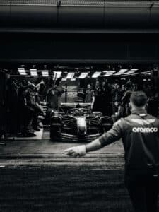 Aston Martin Aramco F1 car under pit garage lights with crew members preparing for a session, capturing the high-pressure atmosphere of the 2026 regulation cycle.