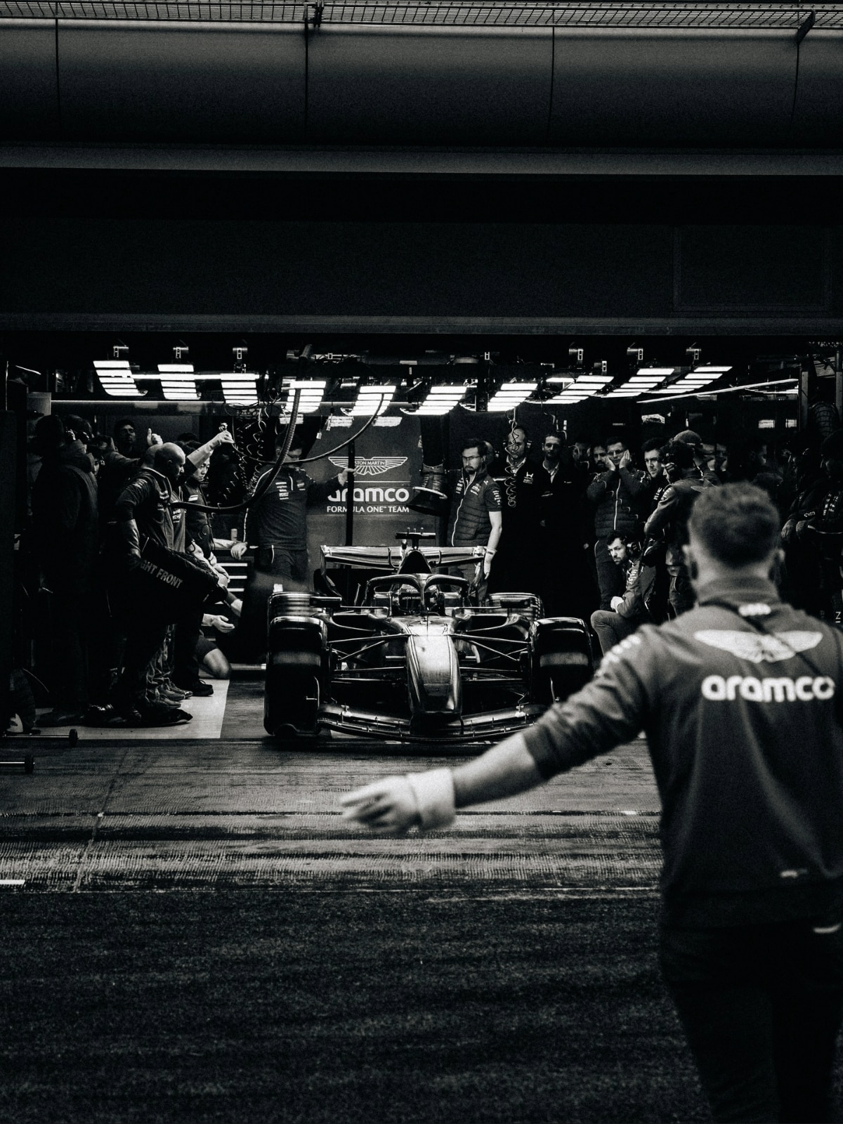 Aston Martin Aramco F1 car under pit garage lights with crew members preparing for a session, capturing the high-pressure atmosphere of the 2026 regulation cycle.