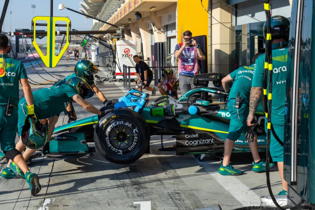 A high-angle view of Aston Martin mechanics crowded around the AMR26 in the Bahrain garage, working on the Honda power unit during a reliability-limited session.