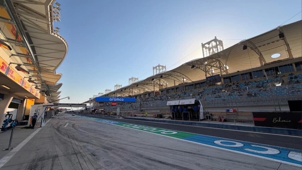 A wide-angle view of the Bahrain International Circuit main straight and grandstands under a clear blue sky during the final day of pre-season testing.