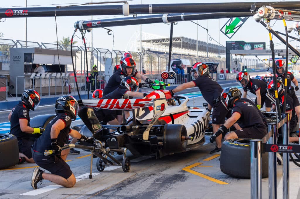 The Haas F1 pit crew performing adjustments on the car in the Bahrain pit lane during the final day of 2026 testing.