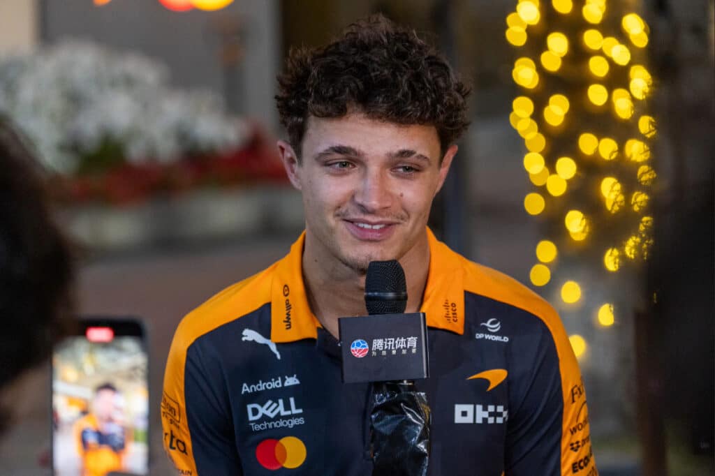 McLaren F1 driver Lando Norris smiling during a media interview at the Bahrain International Circuit, representing the team's internal cohesion.
