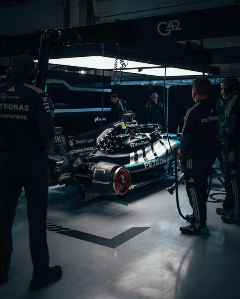 Mercedes-AMG F1 engineers and mechanics observing the W15 chassis in the garage during a technical inspection.