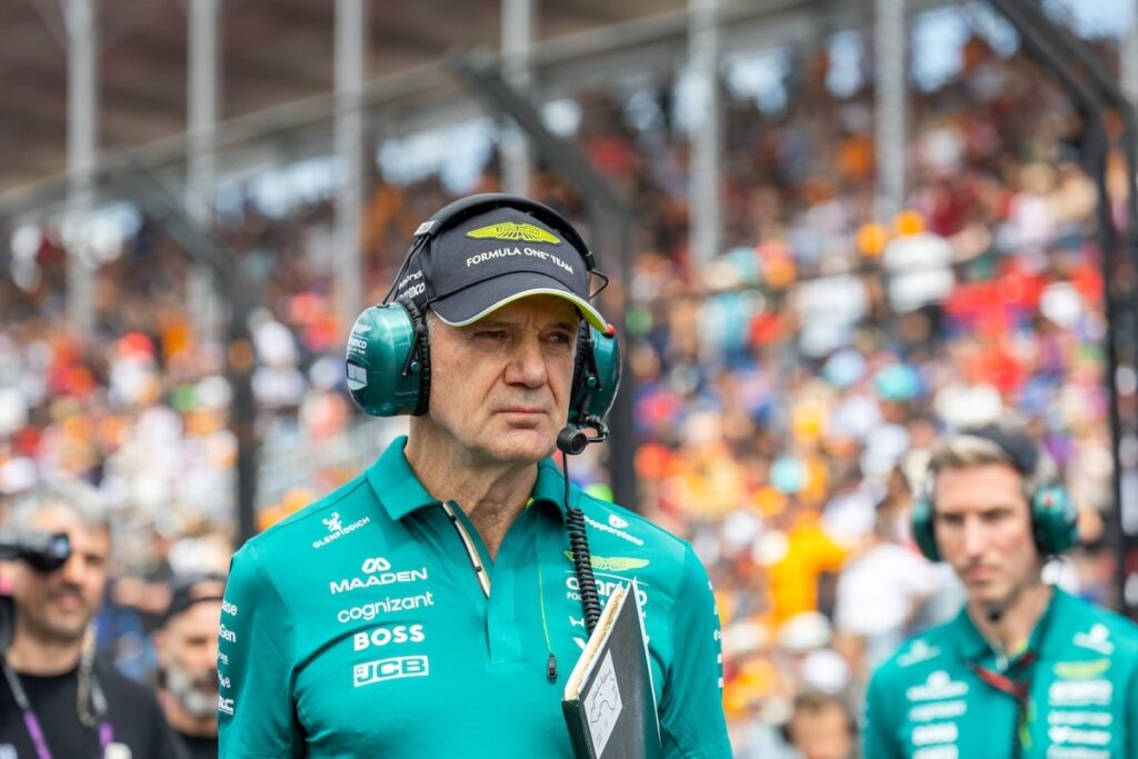 Adrian Newey wearing Aston Martin F1 team kit and headset on the grid, representing the team's long-term strategic technical vision despite 2026 performance challenges.