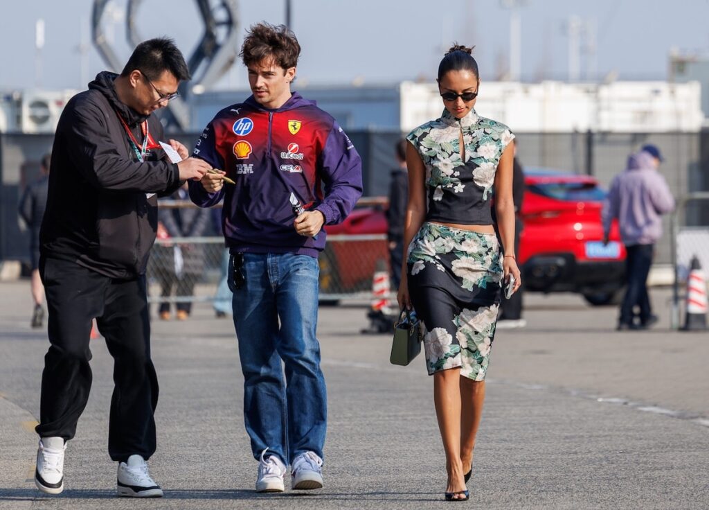 Alexandra Saint-Mleux in a black floral Chinese-inspired outfit walking through the Shanghai paddock with Charles Leclerc.