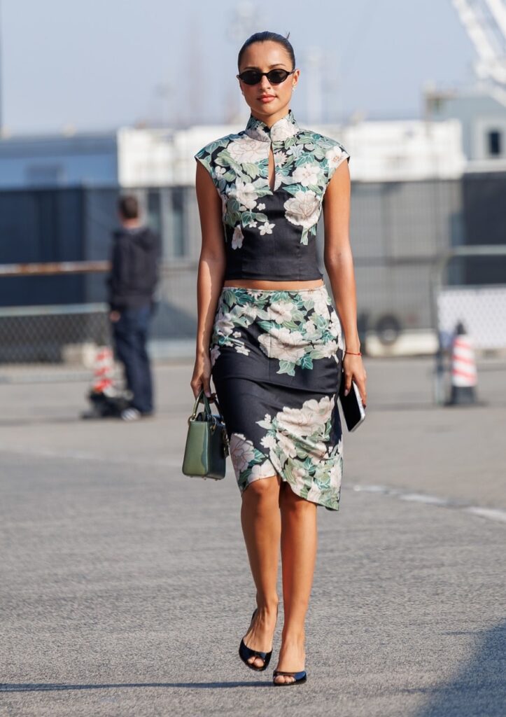A full-length shot of Alexandra Saint-Mleux wearing a black floral qipao-style crop top and skirt at the 2026 Chinese Grand Prix.