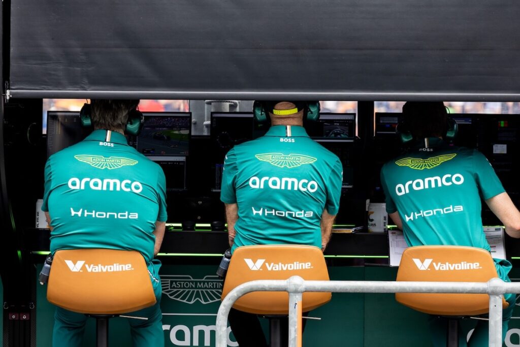 Three Aston Martin F1 team members in green team gear monitor data screens at the pit wall, illustrating the operational leadership roles affected by gardening leave transitions.