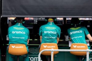 Three Aston Martin F1 team members in green team gear monitor data screens at the pit wall, illustrating the operational leadership roles affected by gardening leave transitions.