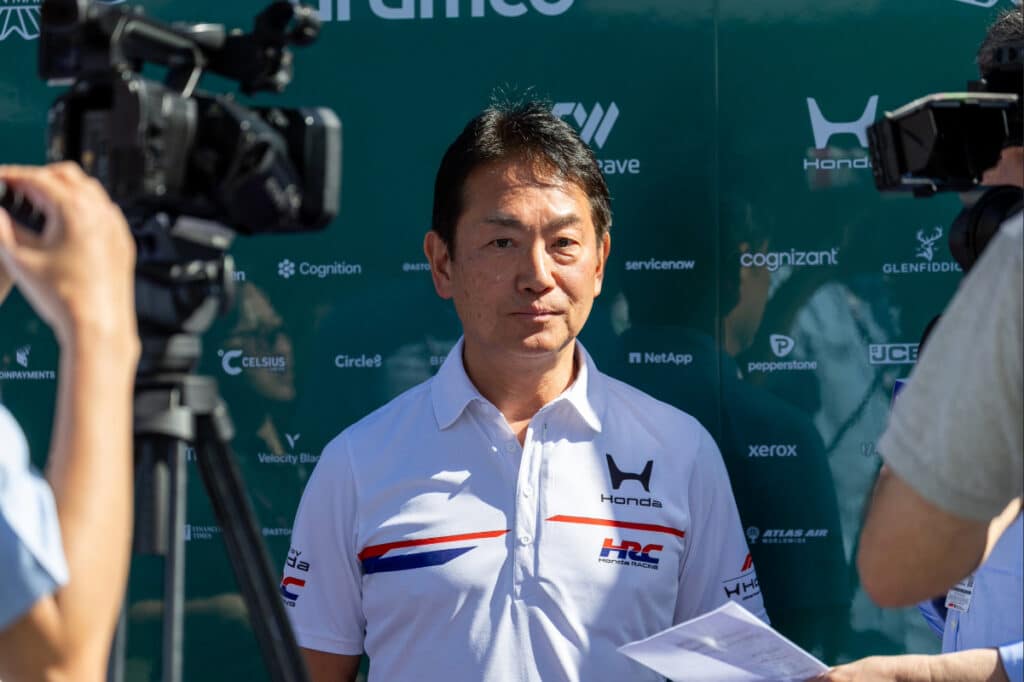 Honda Racing President Koji Watanabe being interviewed by media at the Aston Martin hospitality unit regarding 2026 engine vibrations.
