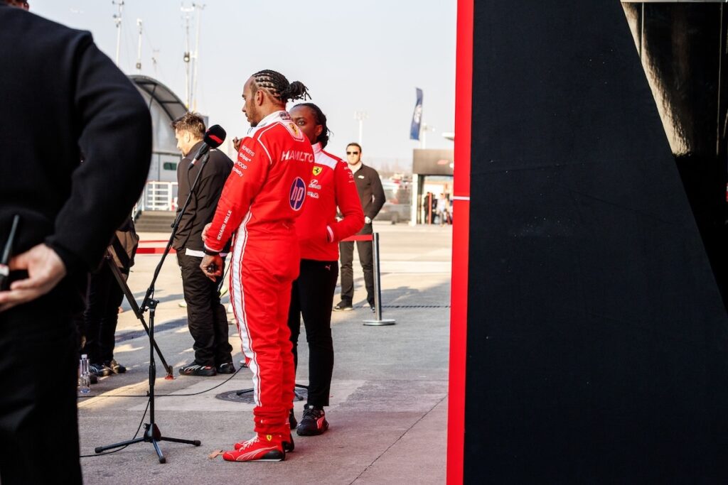 Lewis Hamilton in his red Ferrari racing suit standing in the paddock during the 2026 Chinese Grand Prix weekend.