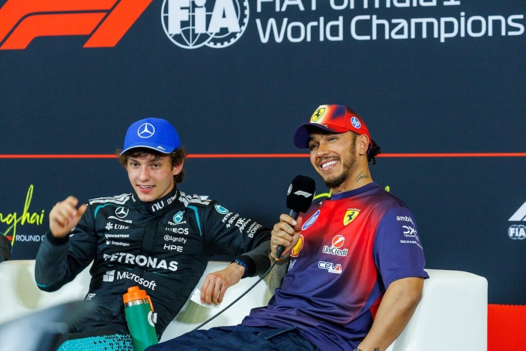 Lewis Hamilton in his Ferrari team kit smiling alongside Mercedes driver Kimi Antonelli during a 2026 Chinese Grand Prix press conference.