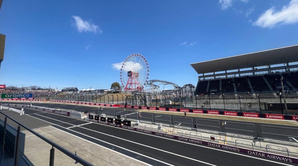 A wide view of the Suzuka Circuit in Japan featuring the iconic Ferris wheel and main grandstand under a clear blue sky.